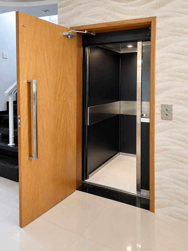 Elevador Tonela com porta de madeira e cabine preta com faixa de inox