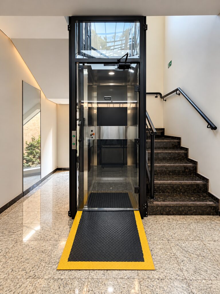 Plataforma de acessibilidade Tonela com cabine de vidro ao lado da escada do hall